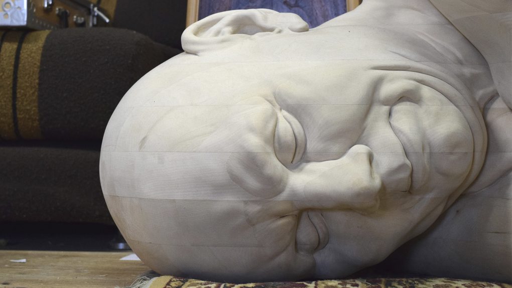 Lähikuva lattialla makaavan puuveistoksen päästä.