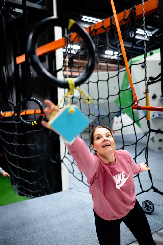 Yksi ryhmän jäsen tavoittelee kädellään ylhäällä renkaassa roikkuvaa palikkaa Wasa Up kiipeilymaailmassa