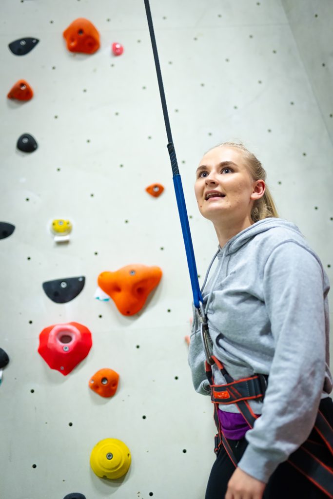 Yksi ryhmän jäsen on valmiina kiipeämään valjaisiin pukeutuneena Wasa Up kiipeilyseinän vieressä