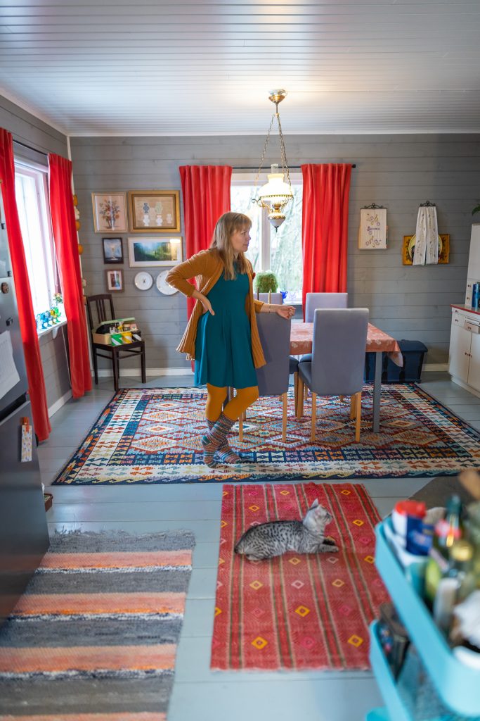 Johanna seisoo ruokailuhuoneessa, jonka seinät on päällystetty siniharmaaksi maalatulla raakalaudalla