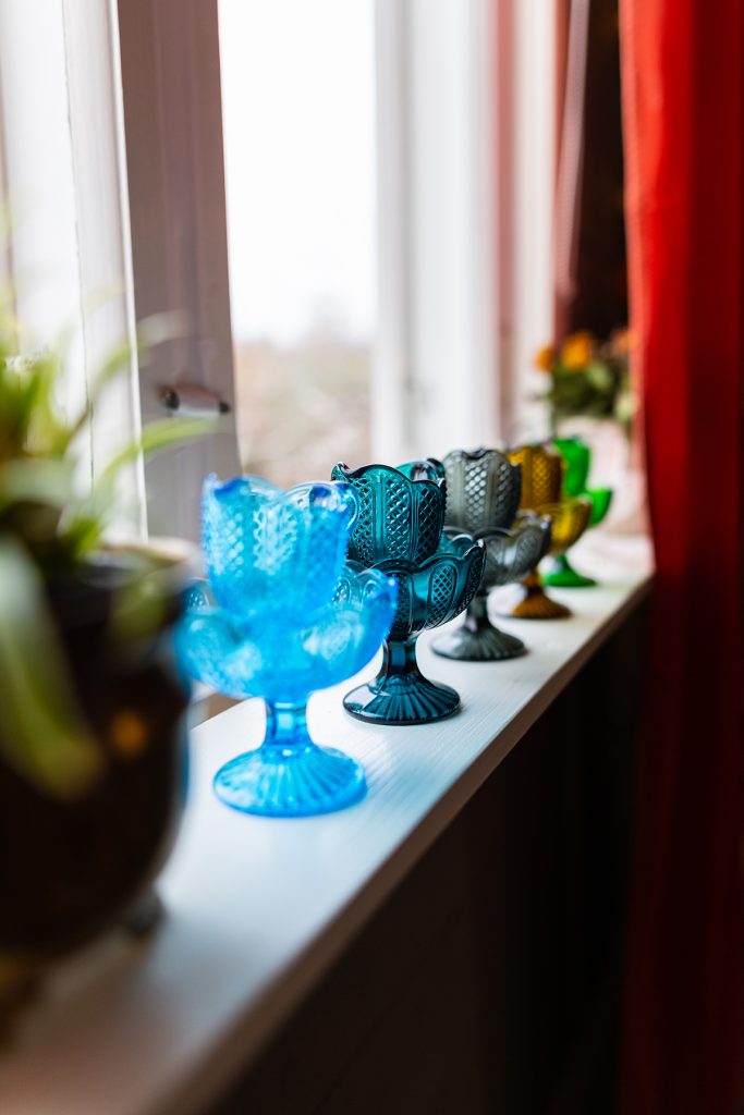 Vanhoja lasisia värikkäitä kermakkoja ja sokerikkoja ikkunalaudalla