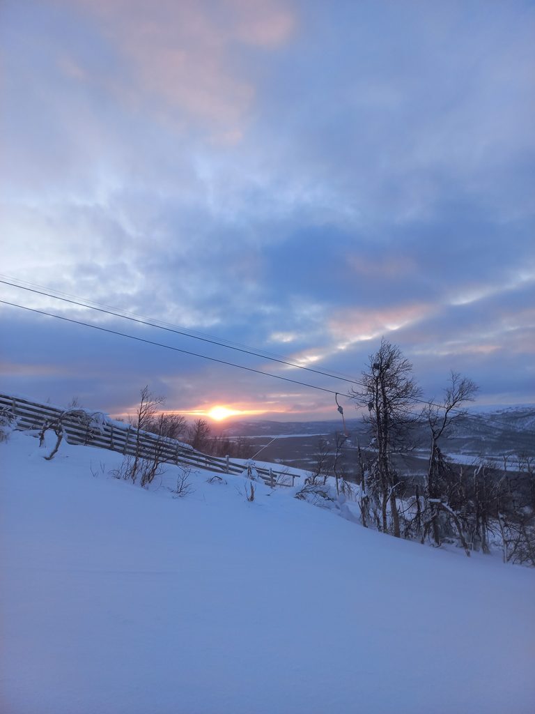 Aurinko nousee taivaanrannasta, kuvassa myös rinnettä