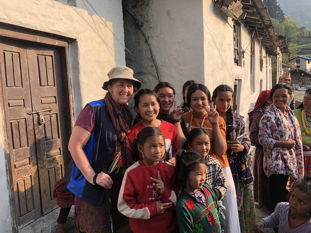 Nainen ja tyttöjä seisoo ulkona rakennuksen edessä ja katsoo kameraan hymyillen